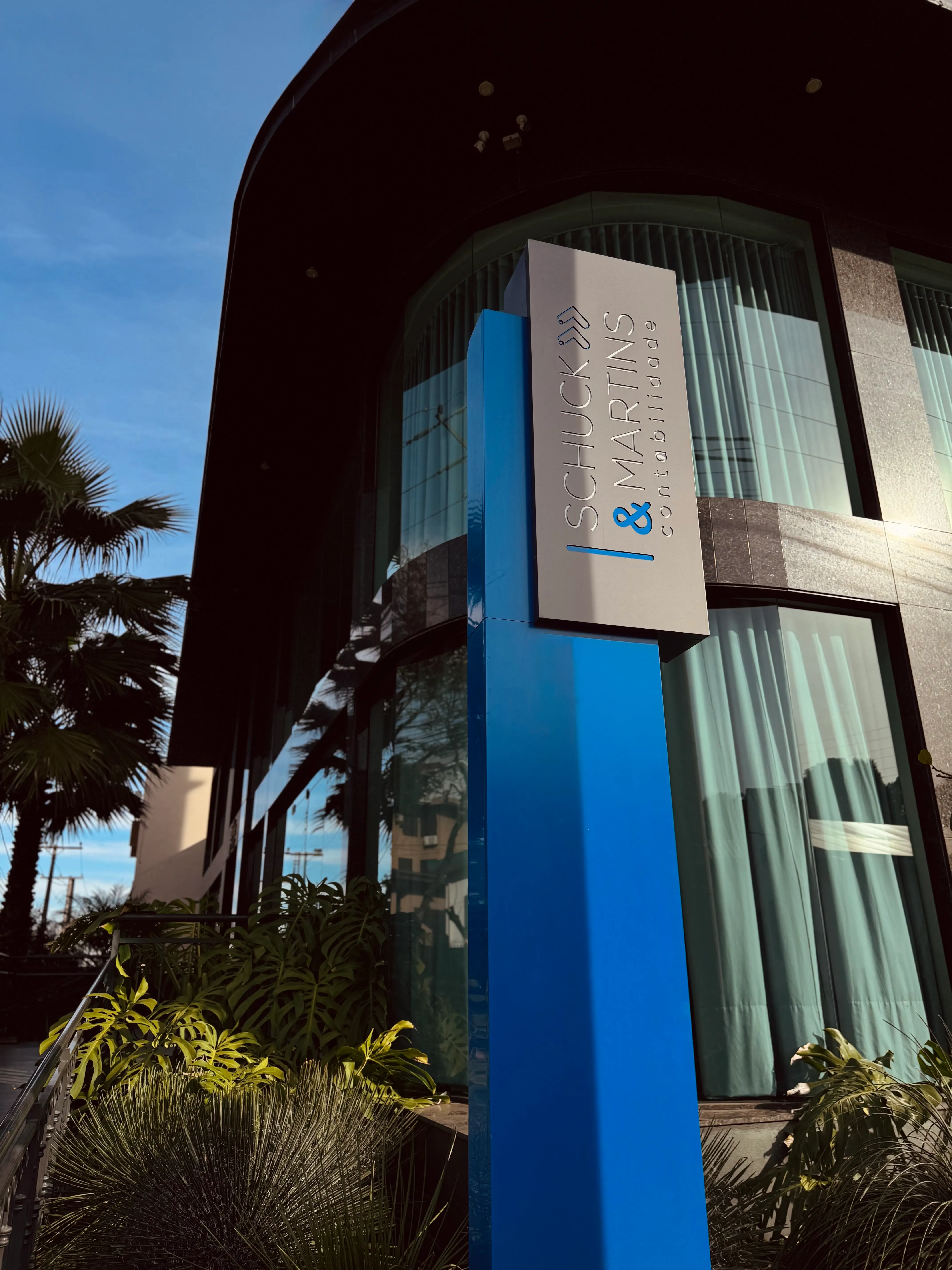 Totem azul da Schuck & Martins em frente à fachada de vidro da nova sede